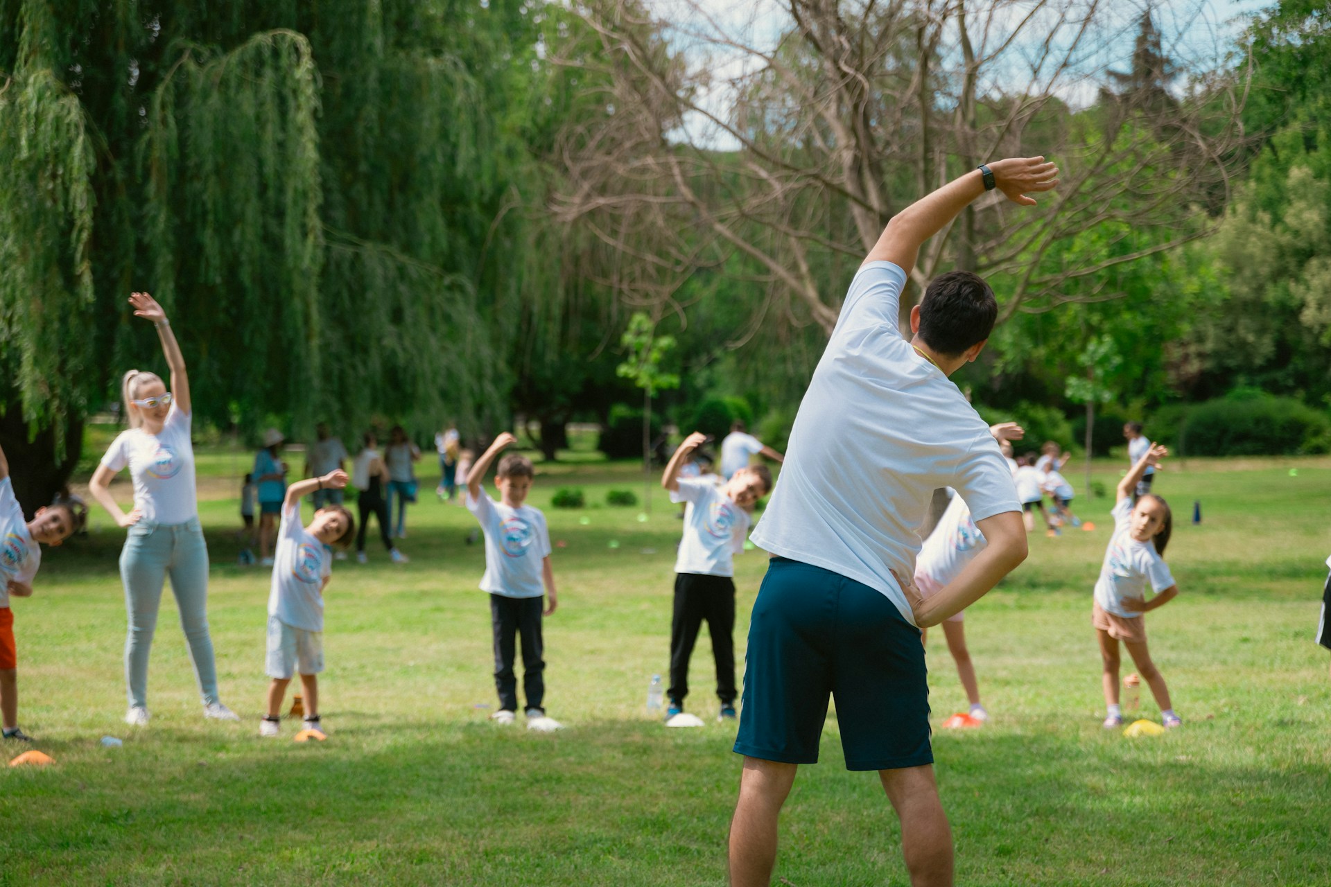 Children stretching in a green field guided by
an instructor.